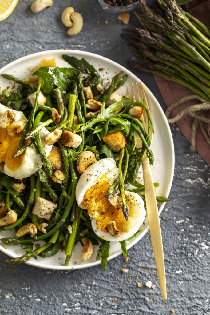 Insalata di asparagi, rucola, uova e anacardi con pane tostato e vinairette al limone. Piatto finito 